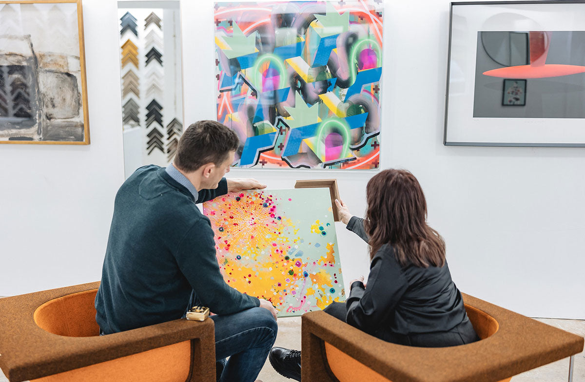 Two people sitting looking at a painted Canvas